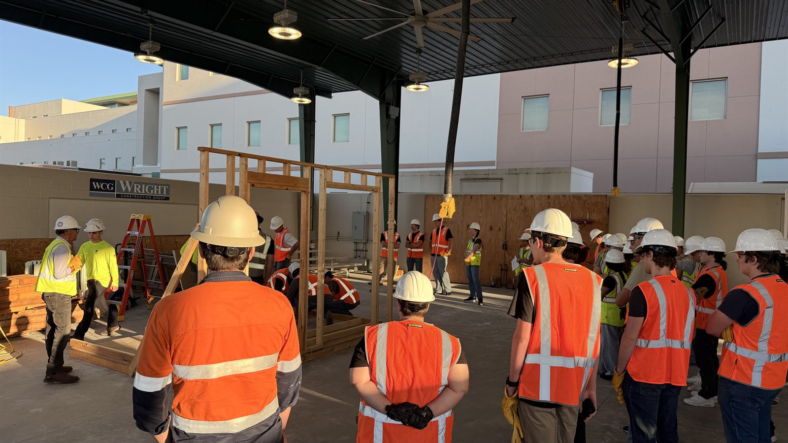 Students and construction professionals gathered around a timber-framing mock-up at the campus training facility