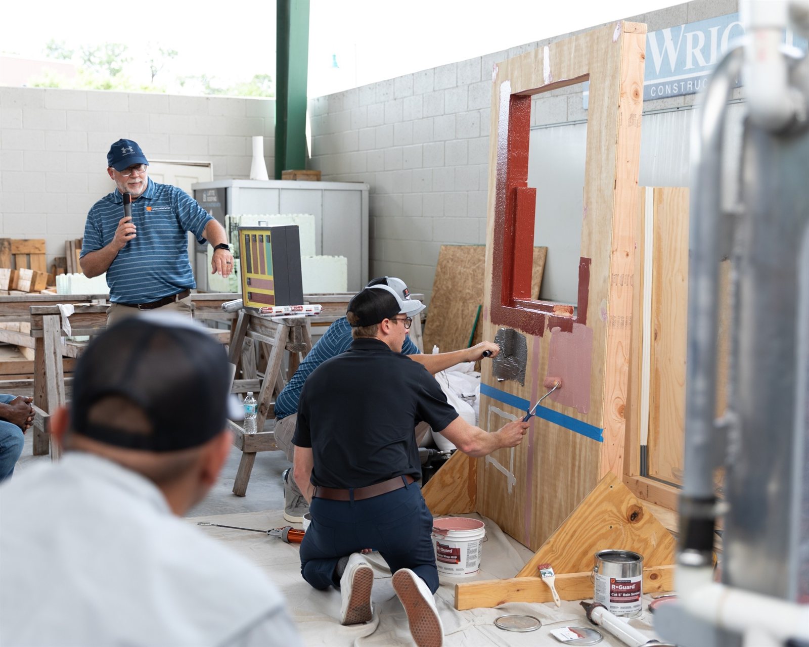 A construction professional explains a wall and window mock-up while another demonstrates building-envelope materials