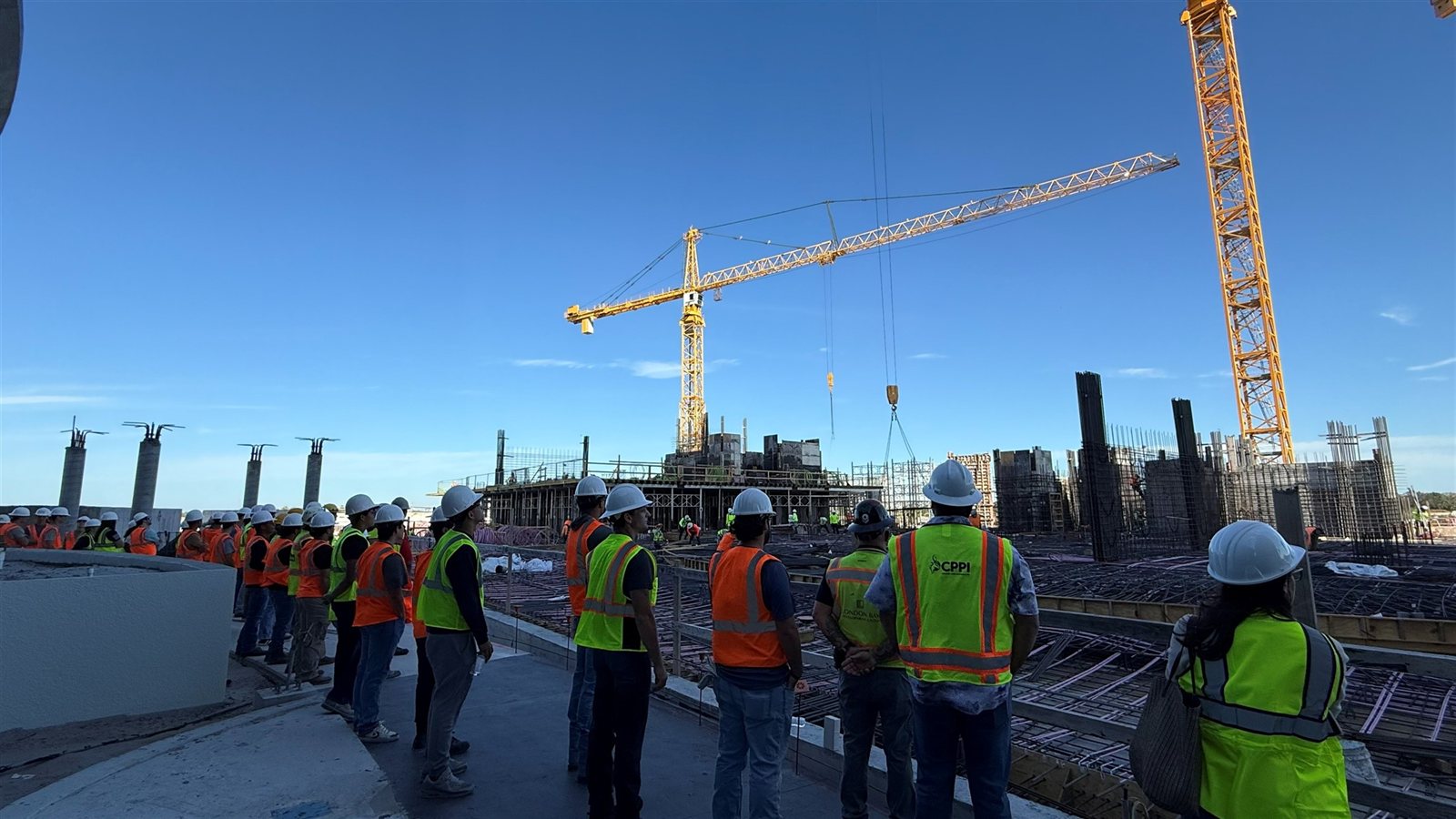 Students observing concrete formwork, reinforcing steel, and tower cranes during a construction site tour