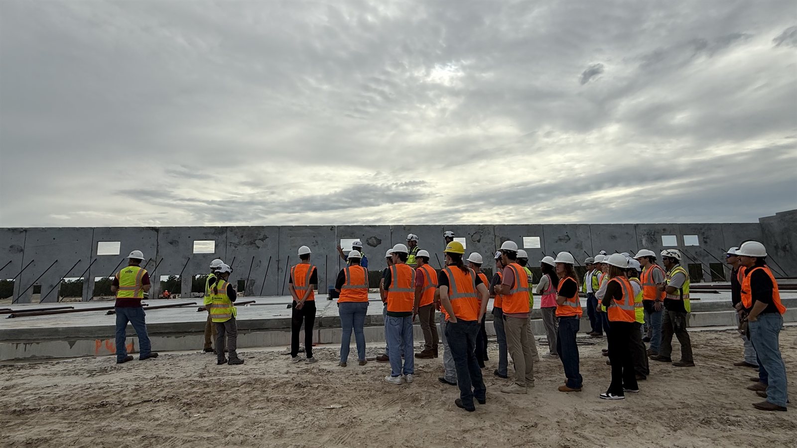 Students listening to a site explanation beside braced concrete wall panels under construction