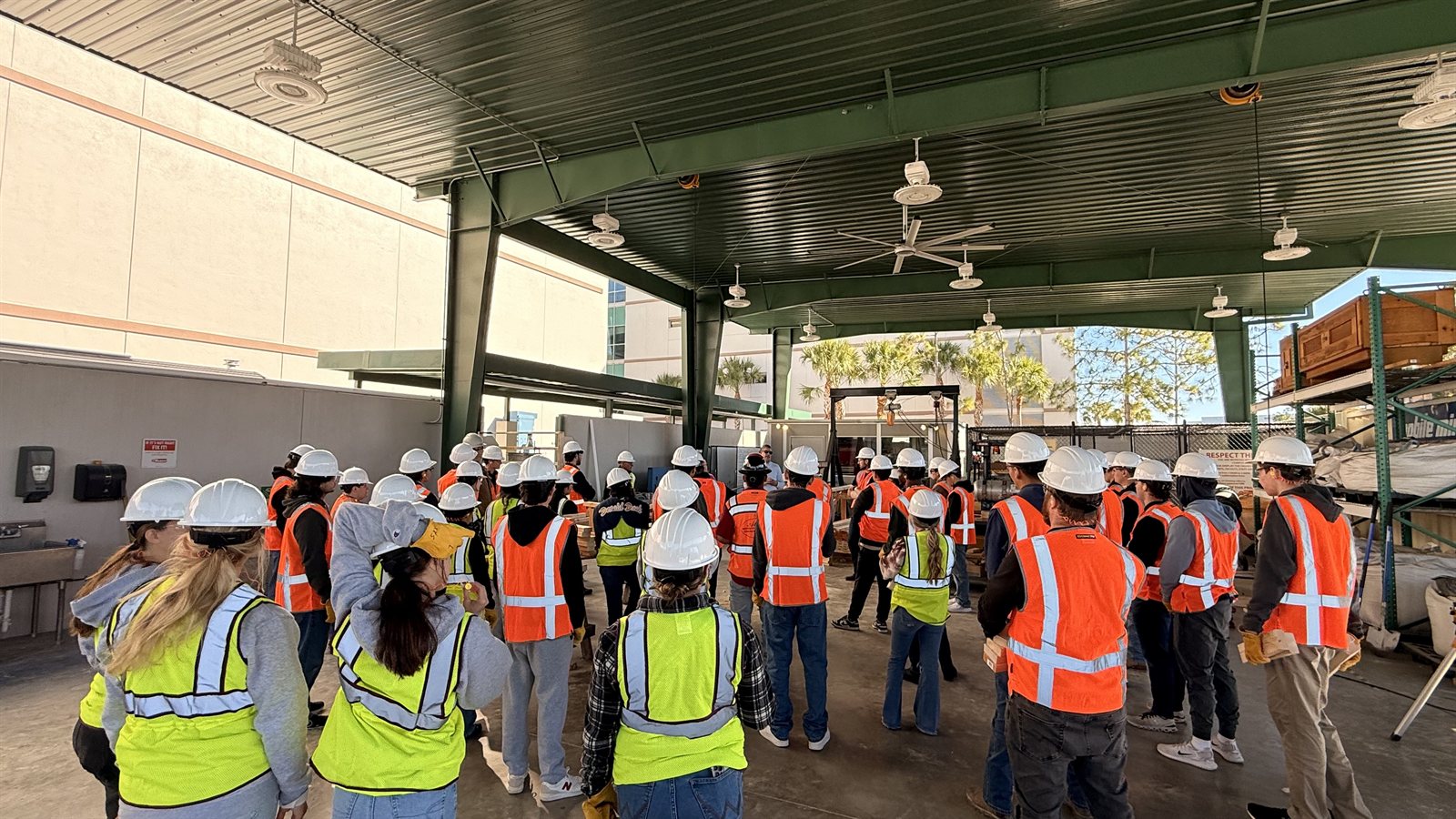 Students in hard hats and safety vests listening to a practical explanation in the construction training facility