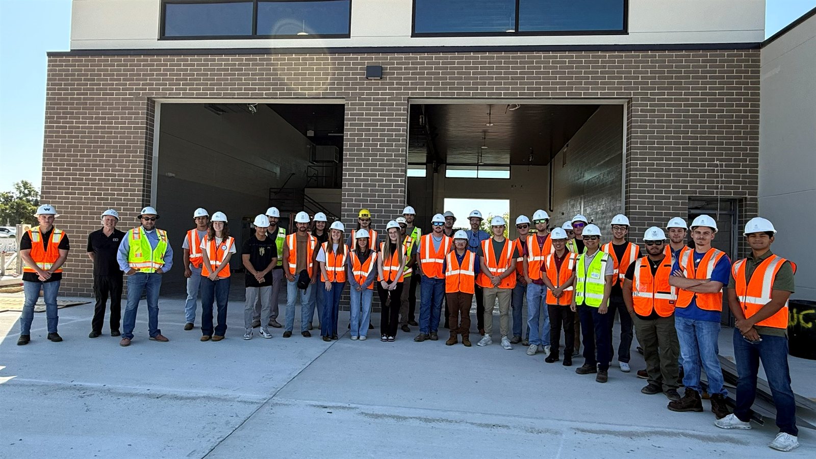 Dr. Nguyen and a construction-learning group wearing hard hats and safety vests outside a campus training facility